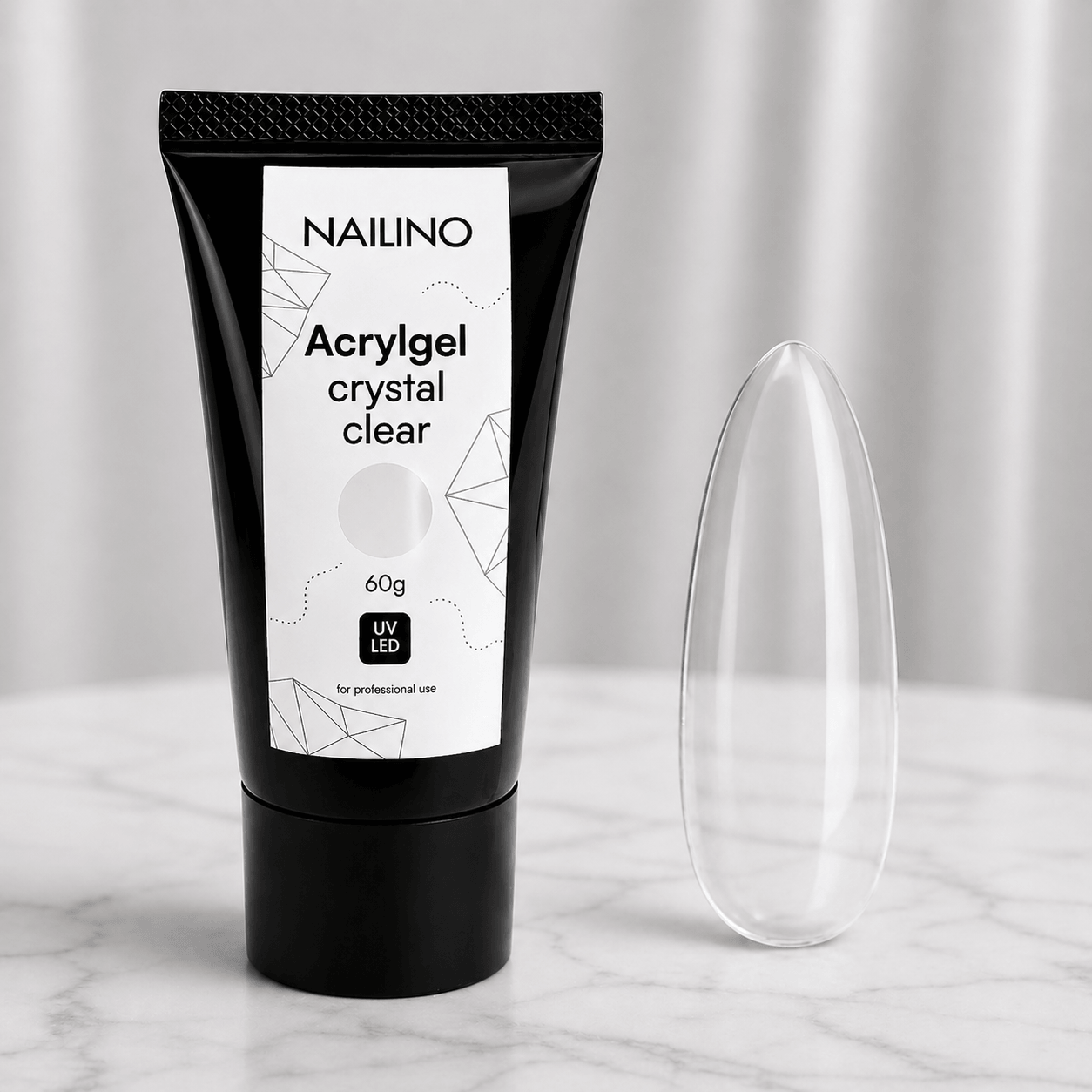 NAILINO Acrylgel Crystal Clear in schwarzer Tube auf einem Marmoruntergrund mit klarer Nagelform.